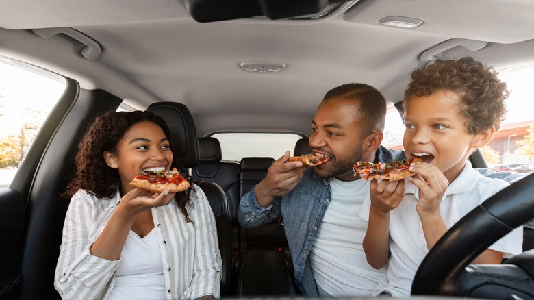 Pai, filha e filho comendo pizza dentro de um carro