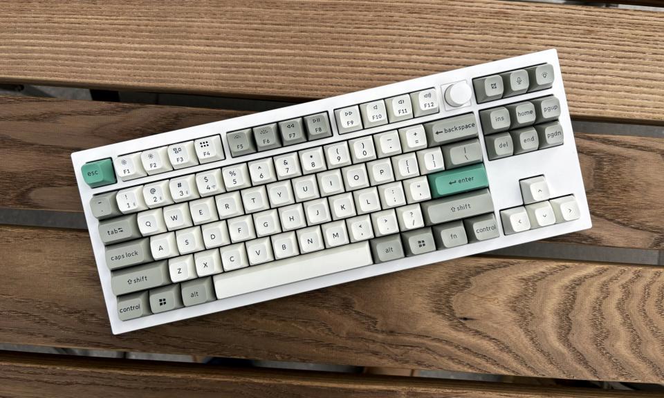 O teclado mecânico Keychron Q3 Max em branco fica em cima de uma mesa externa de madeira marrom.