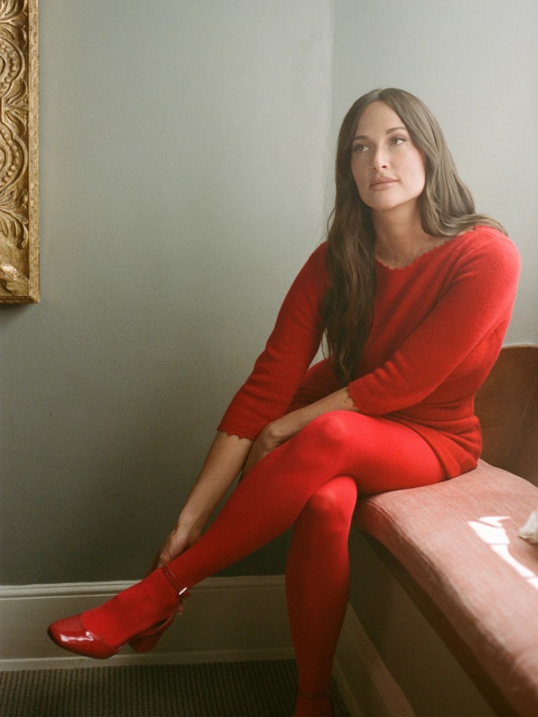 Kacey Musgraves usando minivestido suéter vermelho com meia-calça e salto alto combinando