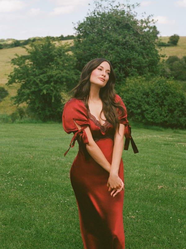 Kacey Musgraves usando vestido de seda vermelho com mangas bufantes e bainha de renda