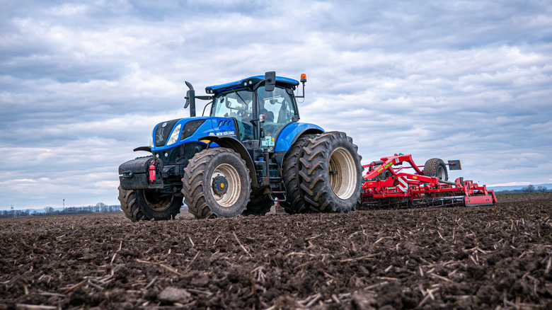 Um trator azul da New Holland atravessando um campo de terra