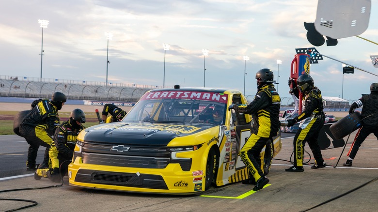 Uma equipe de box trabalha em um caminhão NASCAR Truck Series preto e amarelo no meio de uma corrida.