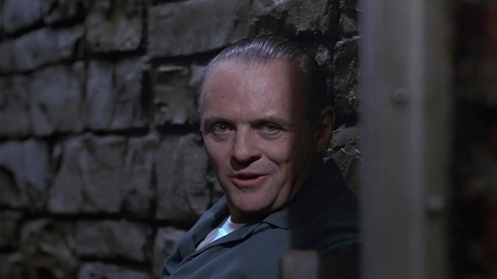 Anthony Hopkins como Hannibal Lecter sorrindo de sua cela em O Silêncio dos Inocentes.