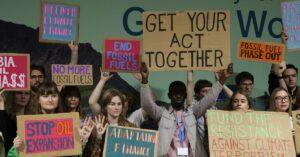 A group of protesters holding signs stand together. One person in the center holds up a sign that says “get your act together.”