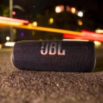 O JBL Flip 6 fica na calçada de uma rua da cidade à noite.