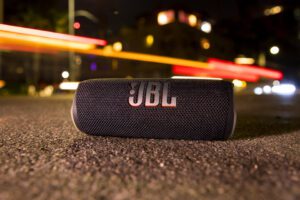 O JBL Flip 6 fica na calçada de uma rua da cidade à noite.