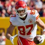 Travis Kelce segura a bola com uma das mãos e corre.