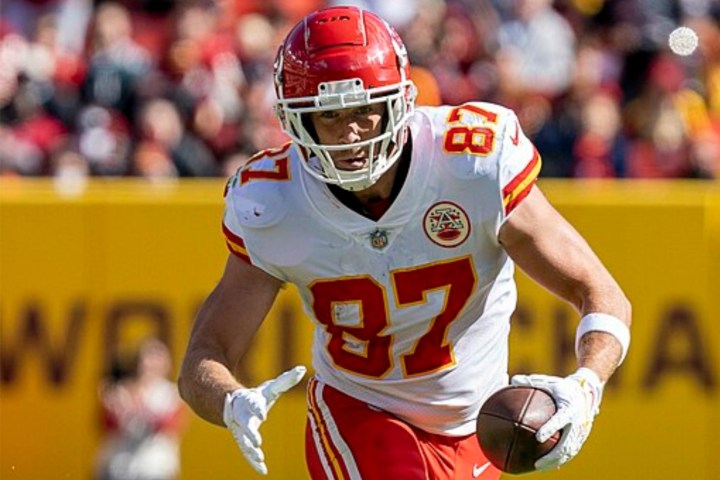 Travis Kelce segura a bola com uma das mãos e corre.