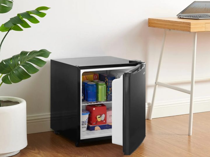 Um 1,7 cu. pés Insignia Mini Fridge situado entre uma planta de casa e uma mesa de laptop.