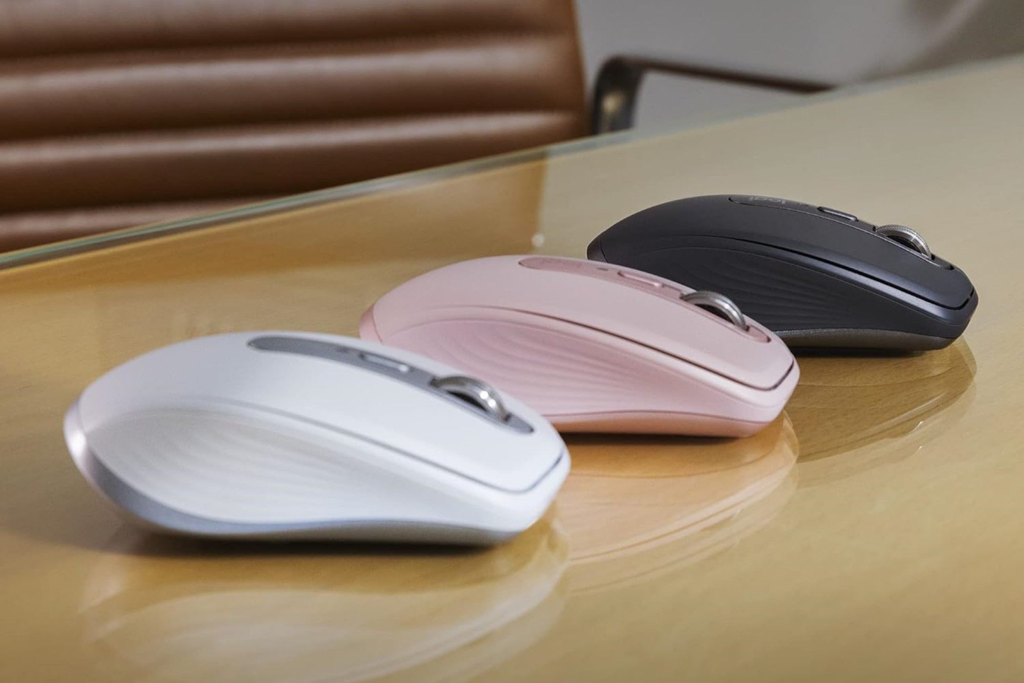 Três variantes do Logitech MX Anywhere 3S sobre uma mesa de vidro