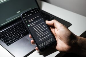 Pessoa usando ChatGPT em um telefone com um laptop em segundo plano