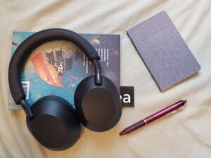 O Sony WH-1000-XM5 em cima de um livro para estudo, ao lado de caderno e caneta.