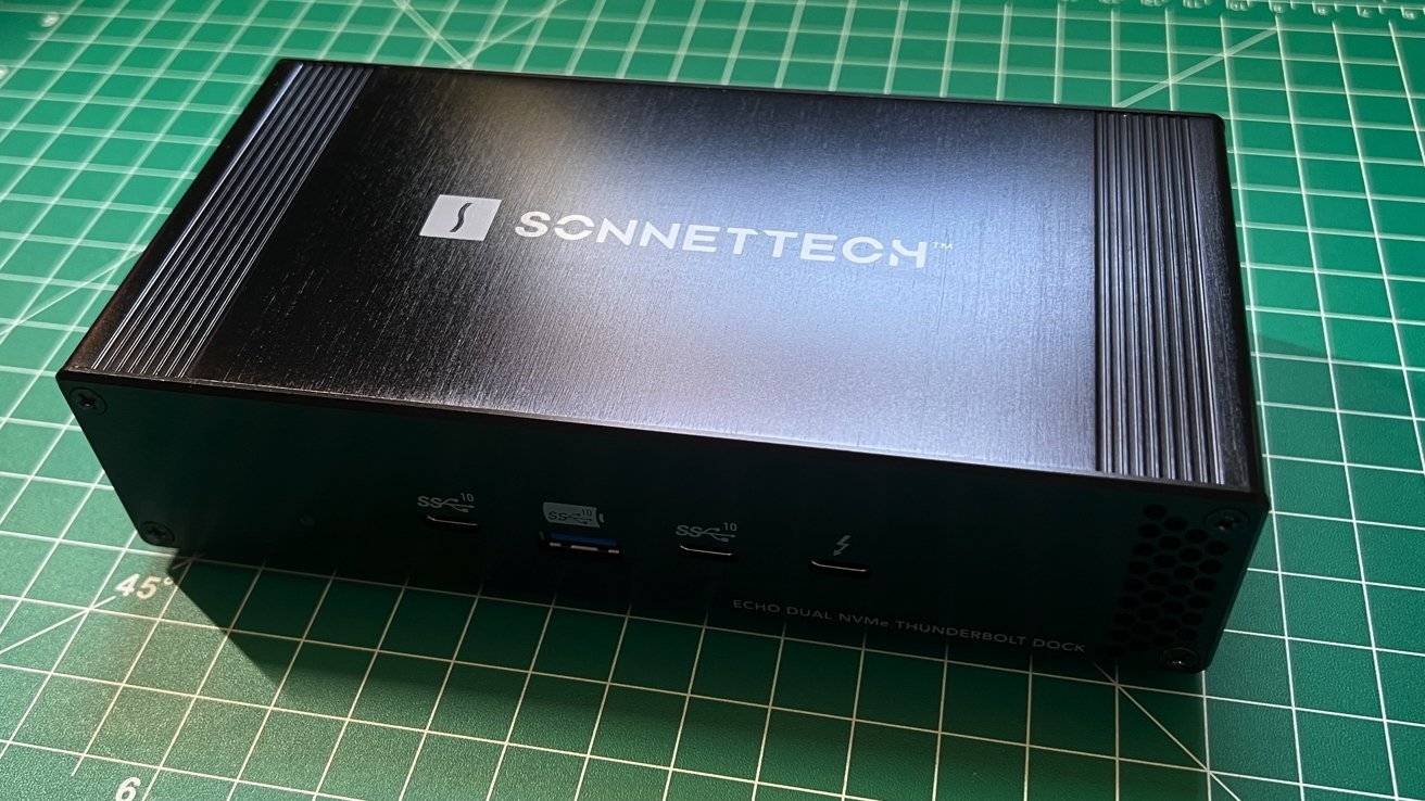 Dock SonnetTech Echo Dual NVMe Thunderbolt preto com múltiplas portas na frente, colocado em uma esteira de corte verde com linhas de grade.