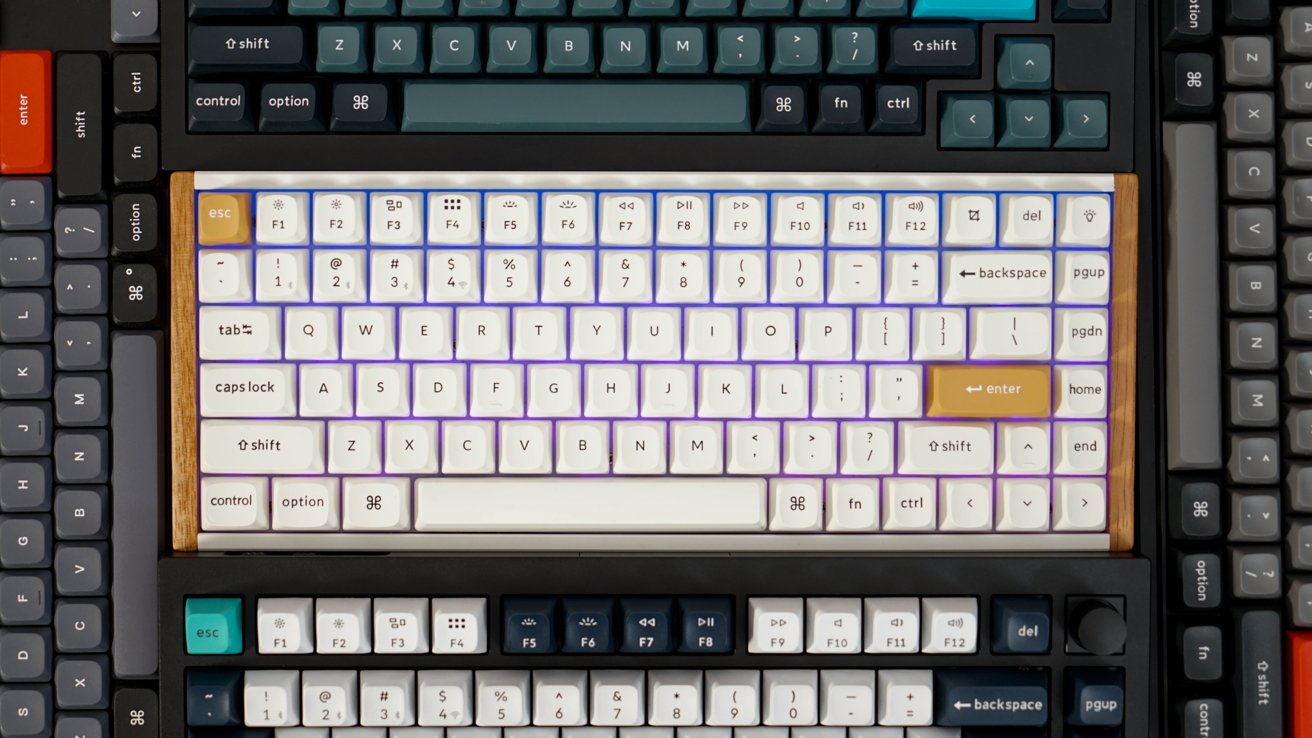 Teclados mecânicos empilhados com teclas de cores variadas, com layouts em branco, verde-azulado e cinza, com detalhes em madeira em um teclado.