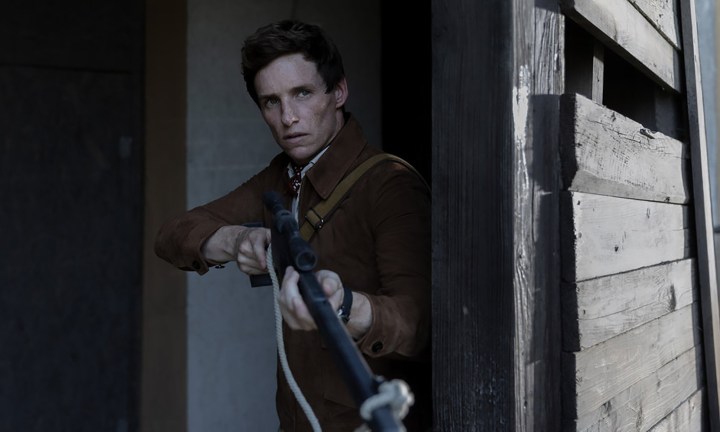 Eddie Redmayne parado em uma porta segurando uma arma em O Dia do Chacal.