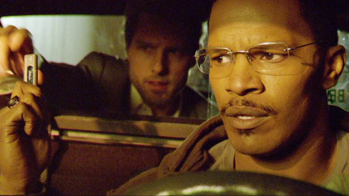 Tom Cruise está sentado no banco de trás de um táxi com Jamie Foxx dirigindo Collateral.