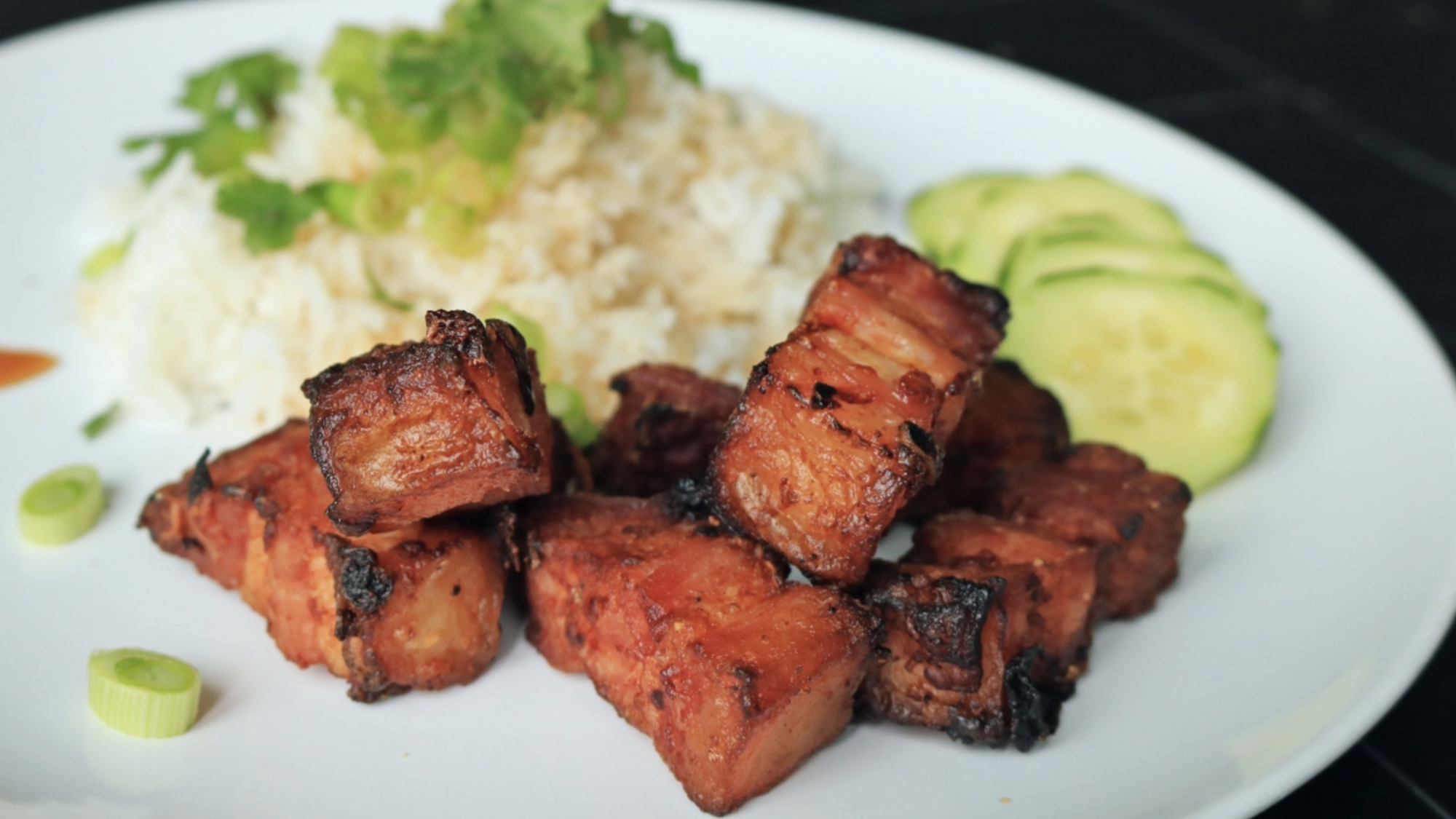 Pedaços de barriga de porco fritos em um prato com arroz e pepino.