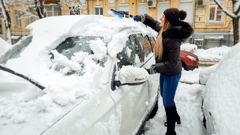 Mulher removendo neve de um carro com uma escova