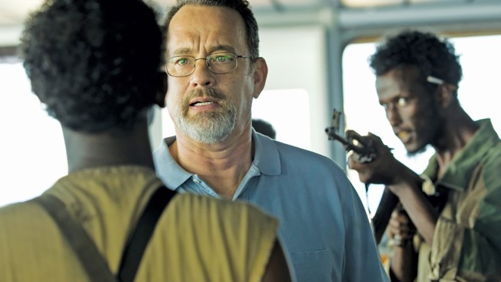 Tom Hanks com uma arma apontada para a cabeça conversando com alguém em uma cena do Capitão Phillips.