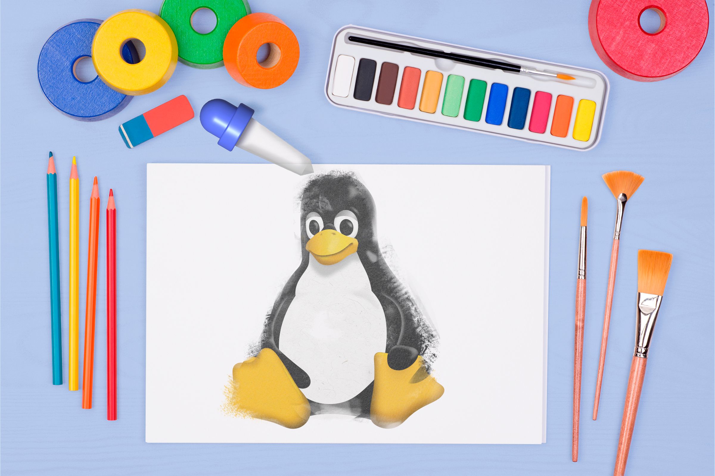 Uma folha de papel com o mascote do Linux e alguns itens de desenho e pintura ao redor.