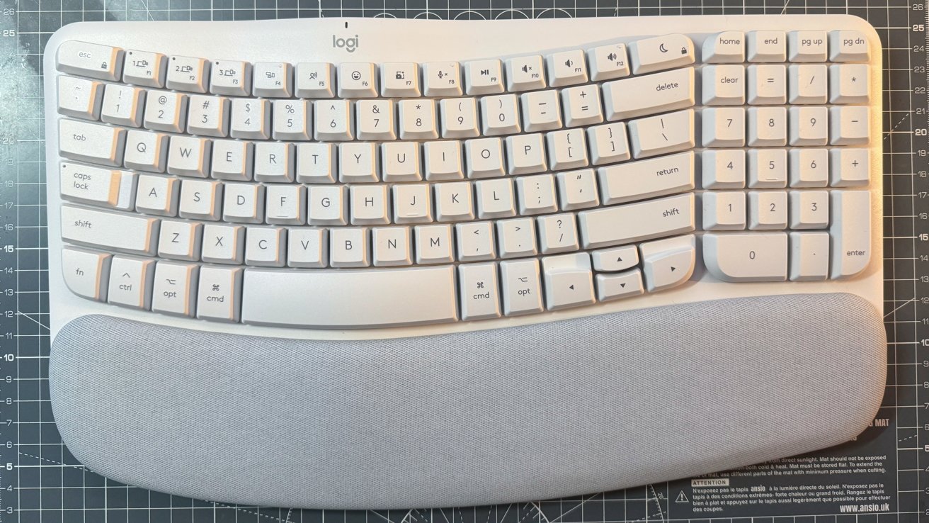 Teclado ergonômico branco com teclas curvas e pousa palmas cinza, colocado em uma superfície com padrão de grade.