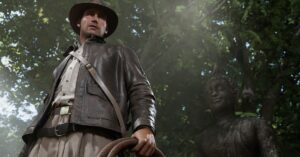 Screenshot from Indiana Jones and the Great Circle featuring a shot of Indiana Jones a white male wearing a brown leather jacket and brown leather hat standing in front of a Buddhist statue.