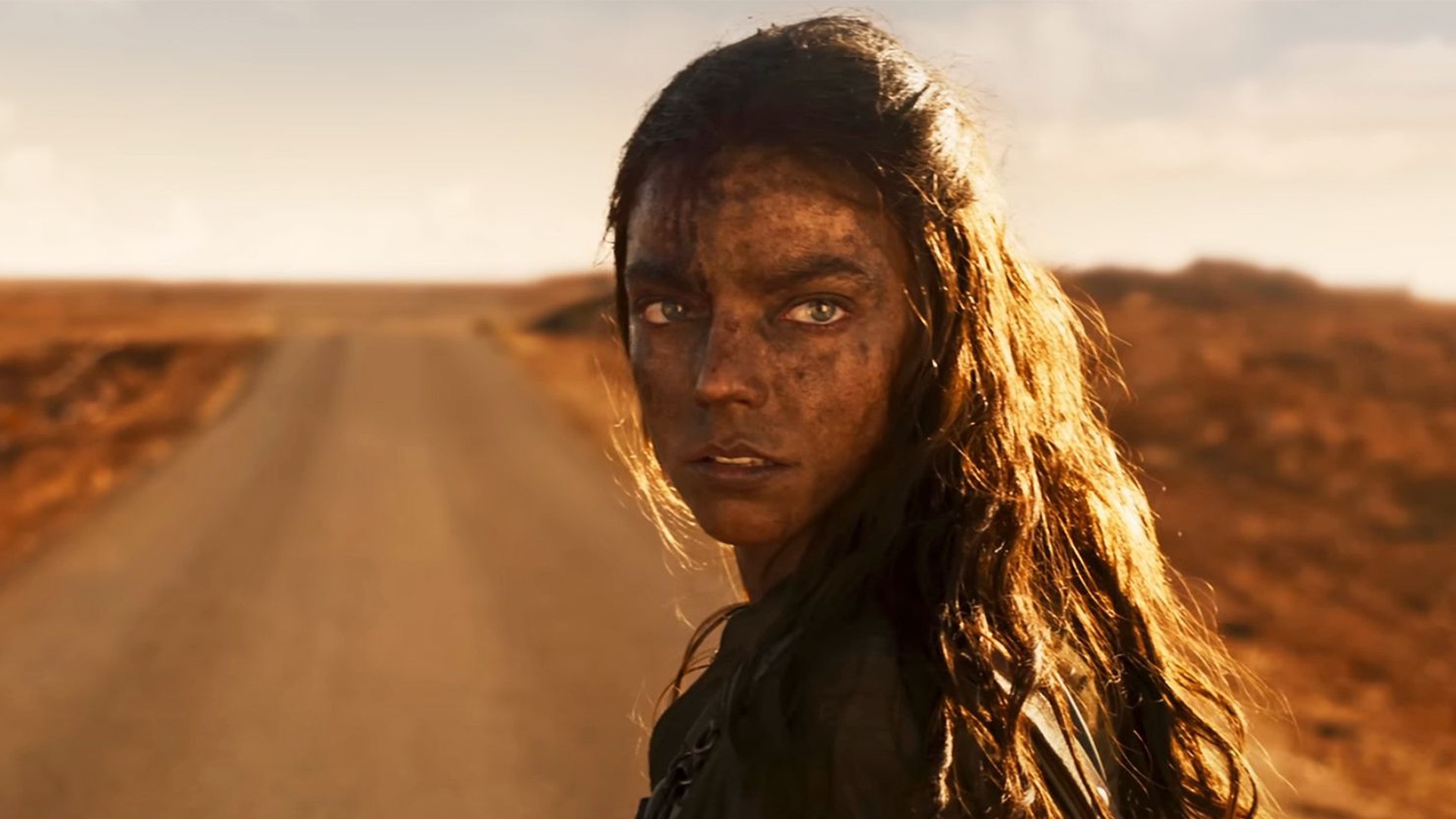 Anya Taylor-Joy está parada em uma estrada empoeirada e olha por cima do ombro em uma foto de "Furiosa: Uma Saga Mad Max."