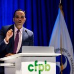 CFPB director Rohit Chopra speaking behind a podium with the green CFPB logo.