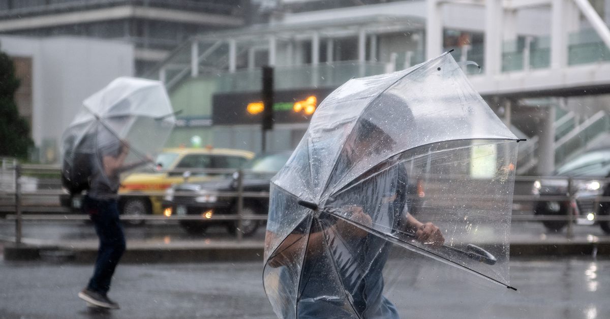 Two people standing in a street shield themselves from rain and snow with clear umbrellas.