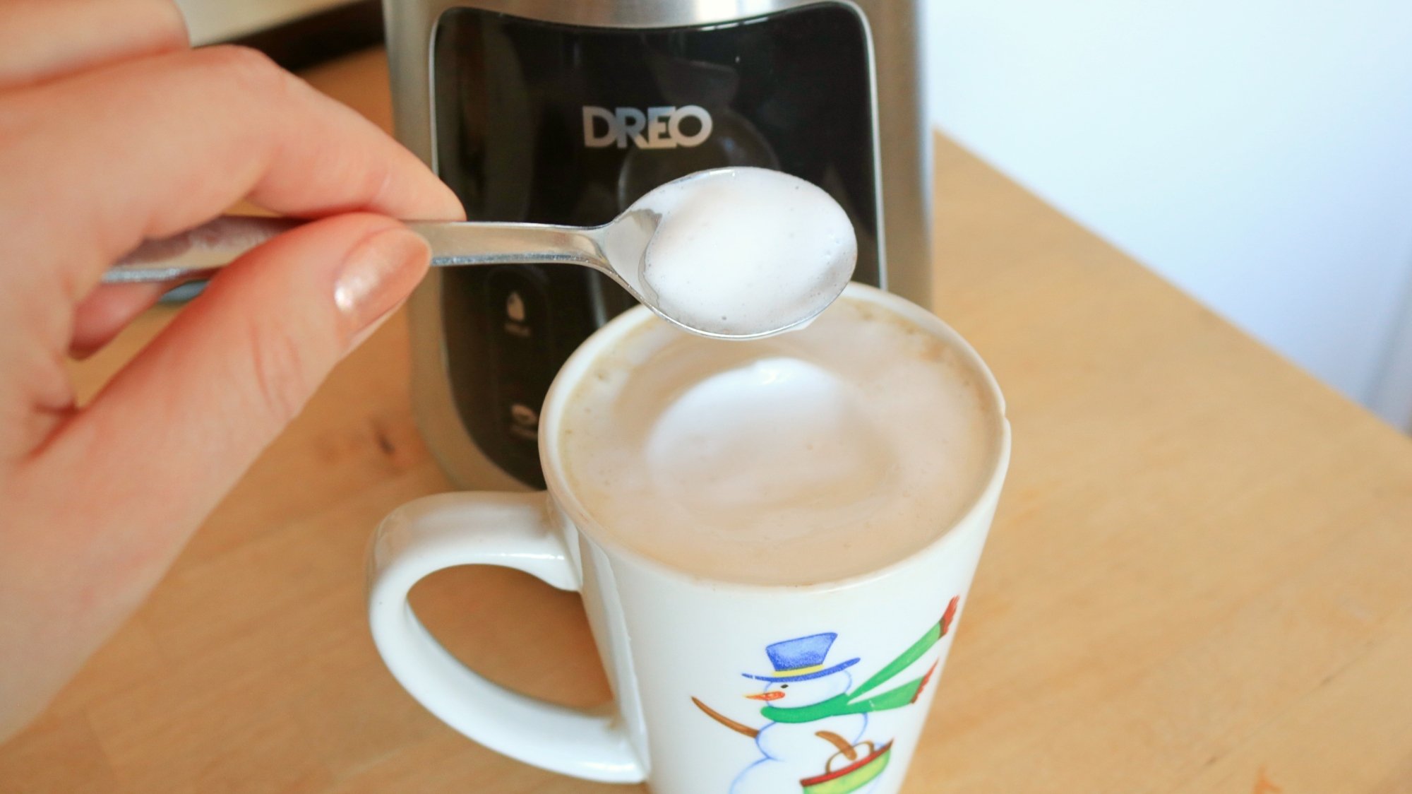 Uma mão tirando espuma de leite de uma xícara de café.