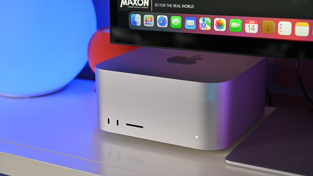 Computador prateado com logotipo da Apple abaixo de um monitor exibindo ícones de aplicativos coloridos cercados por luzes azuis e vermelhas brilhantes em uma mesa.