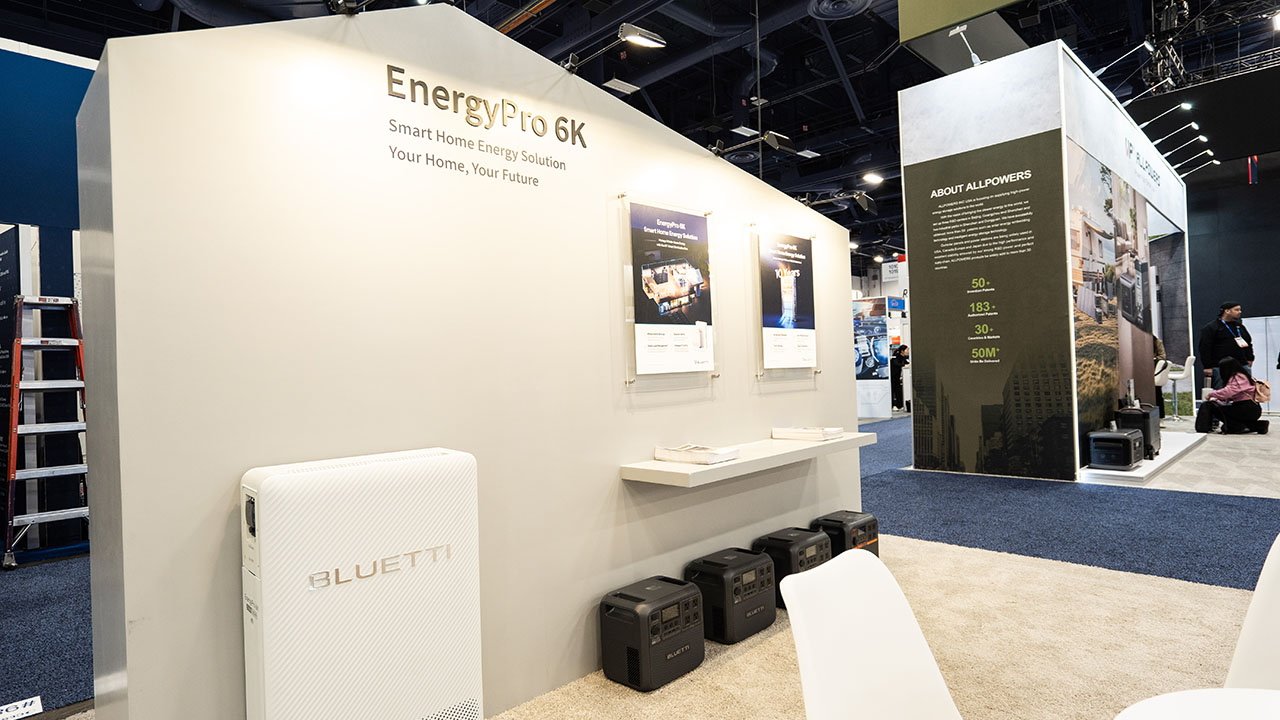 Estande da Bluetti na CES 2025 exibindo soluções de energia para residências inteligentes com pôsteres promocionais, geradores de energia e folhetos em uma prateleira.