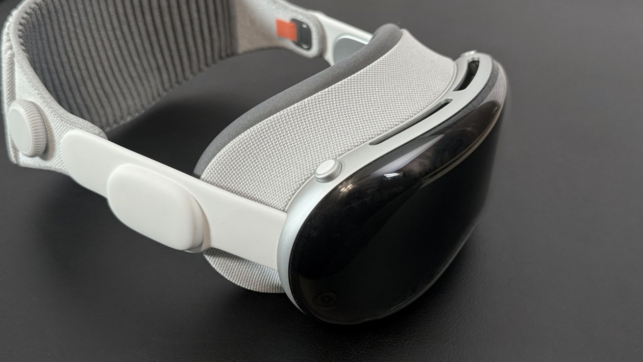 Um elegante headset de realidade virtual com uma pulseira de tecido branco e frente preta brilhante, apoiado em uma superfície escura.