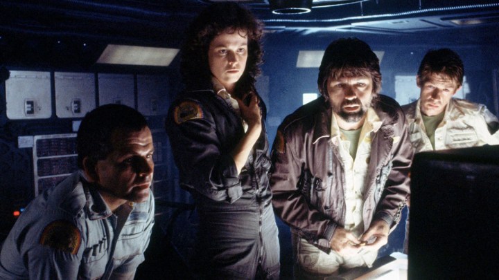 Quatro pessoas se reúnem em torno de um computador enquanto estão em uma nave em Alien.