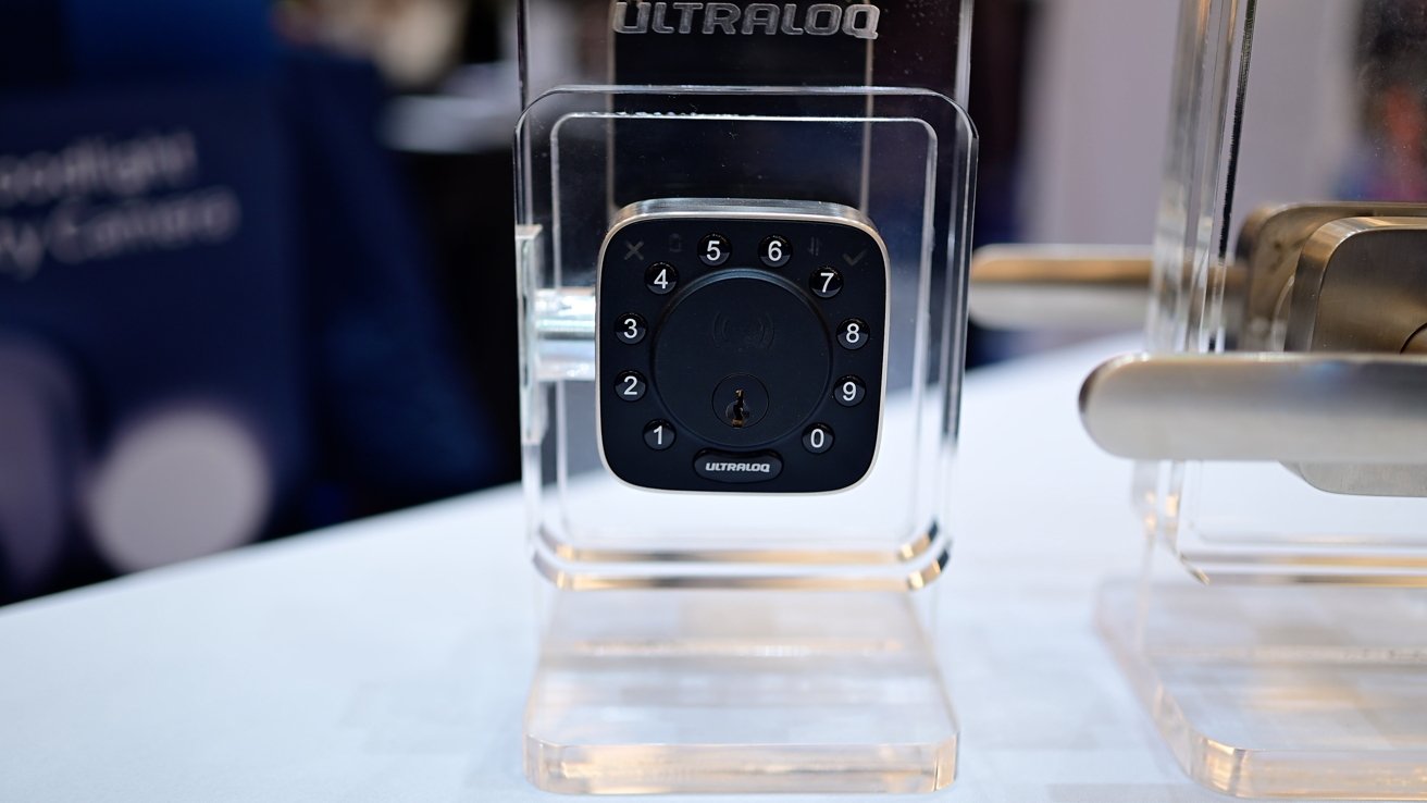 A smart lock with a numeric keypad and keyhole is displayed in a transparent case on a table.