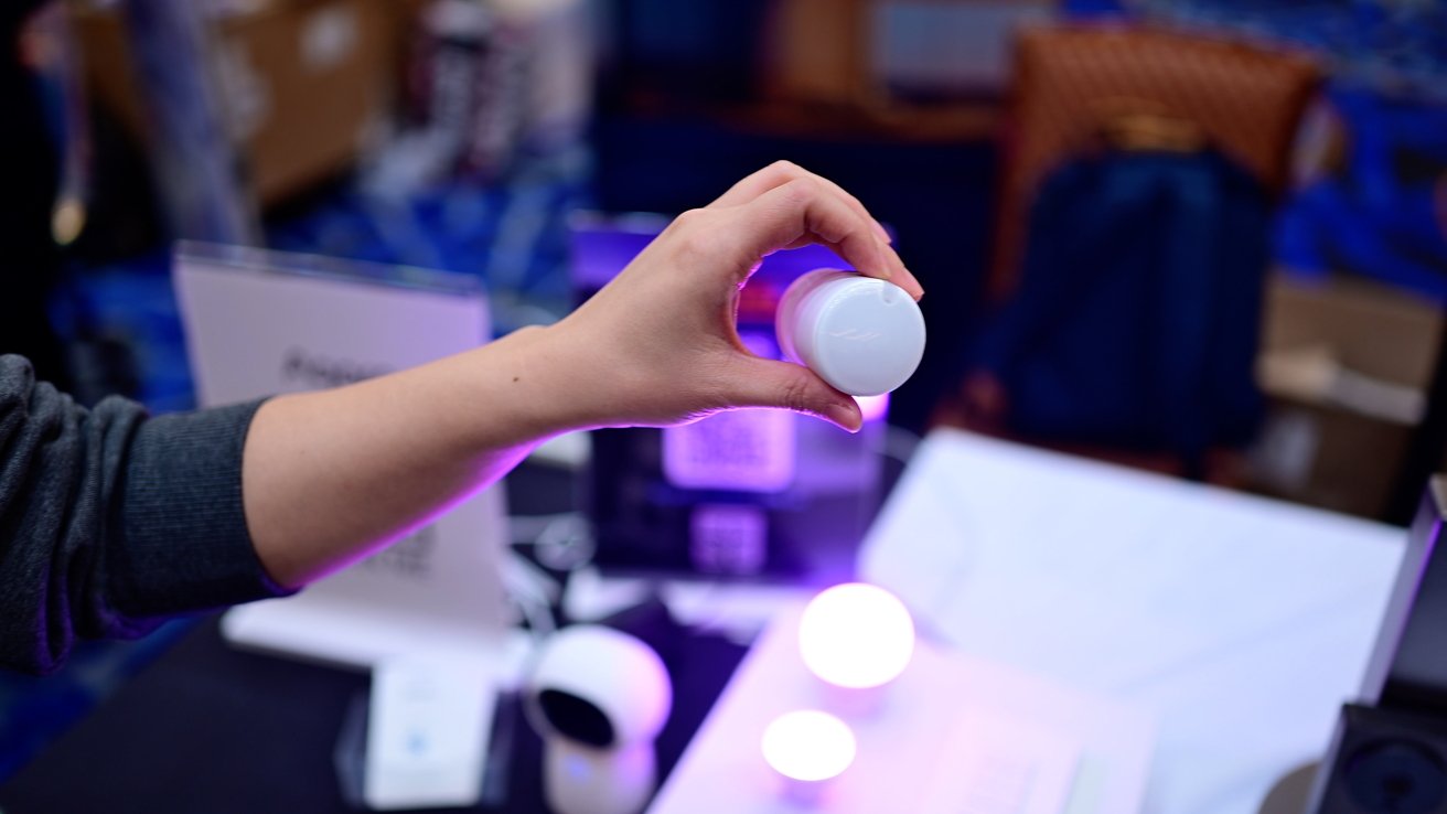 A hand holding a small white cylindrical object above a table displaying glowing orbs in a dimly lit room.