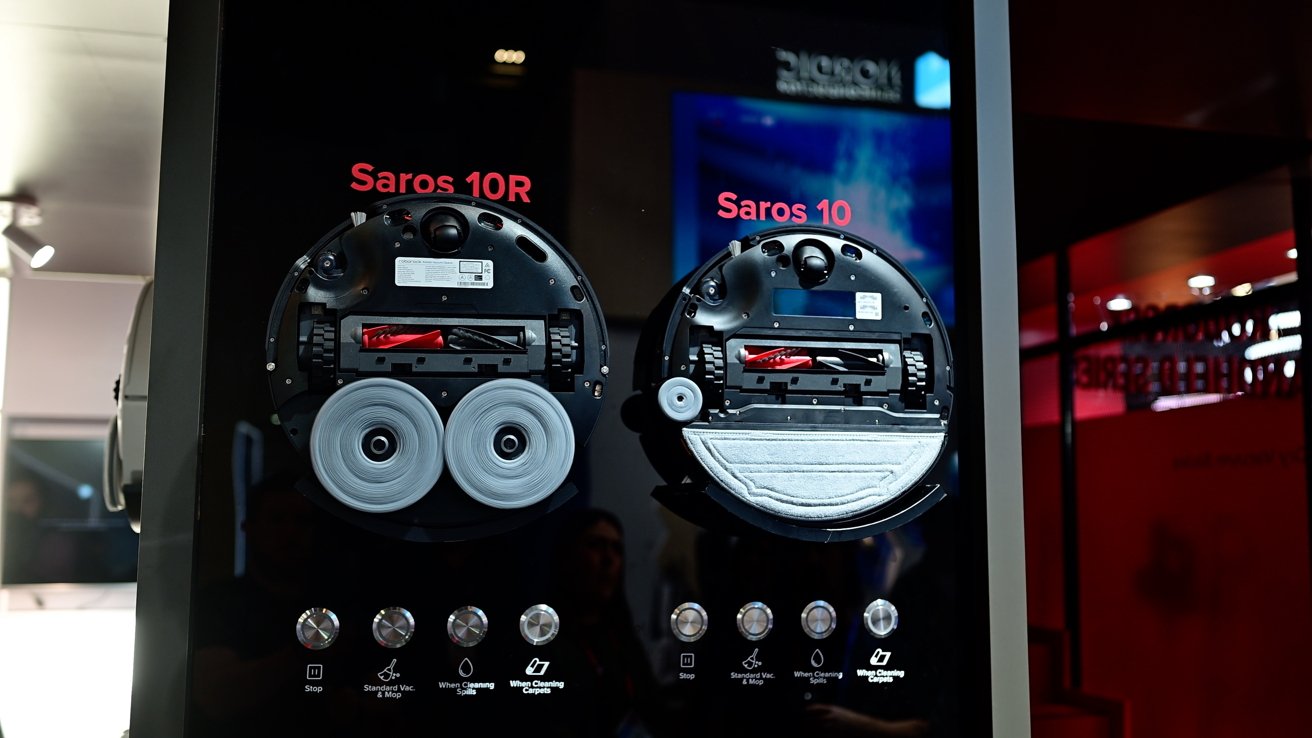 Two black robotic vacuums, labeled Saros 10R and Saros 10, shown from the underside with rollers and brushes, set against a display with various function buttons.