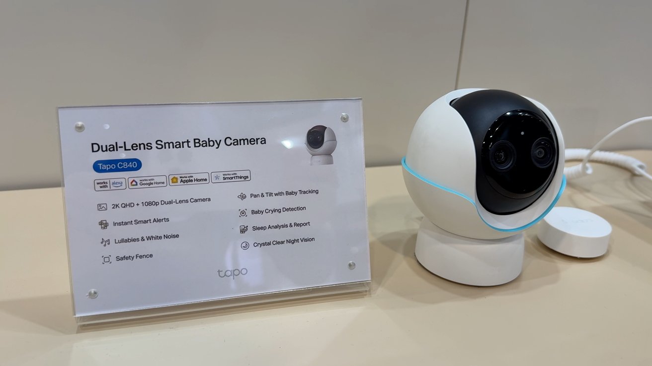 Dual-lens smart baby camera displayed next to a sign listing features like baby tracking, crying detection, sleep analysis, and night vision.