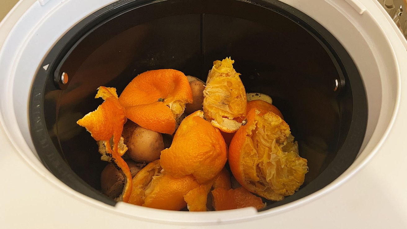 Orange peels and potato skins inside a white compost bin.