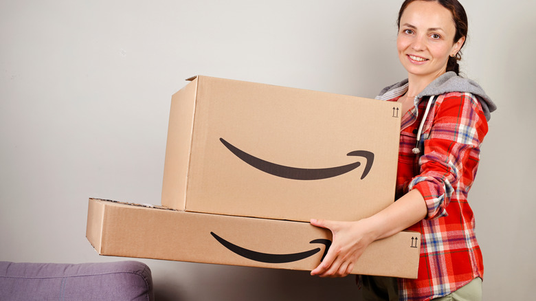 Uma mulher sorridente com cabelos castanhos e um casaco de lã xadrez segura duas grandes caixas da Amazon.