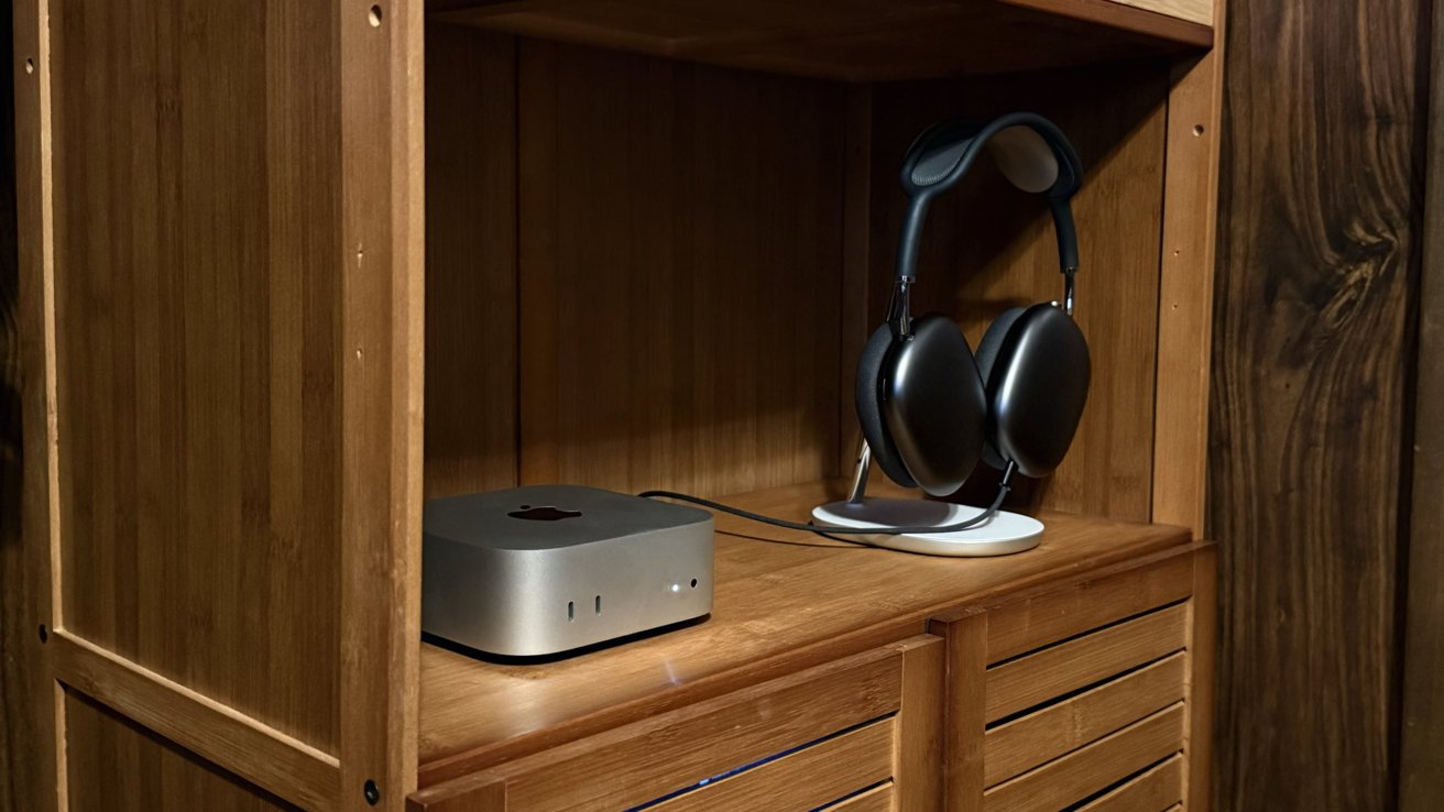 Wooden shelf with a small grey computer, possibly a Mac Mini, and large over-ear headphones on a stand.