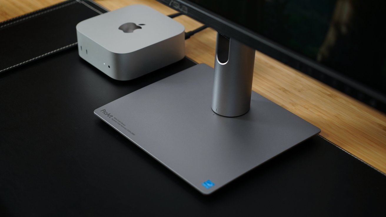 A sleek silver computer next to a monitor stand on a black and wood-textured desk surface.