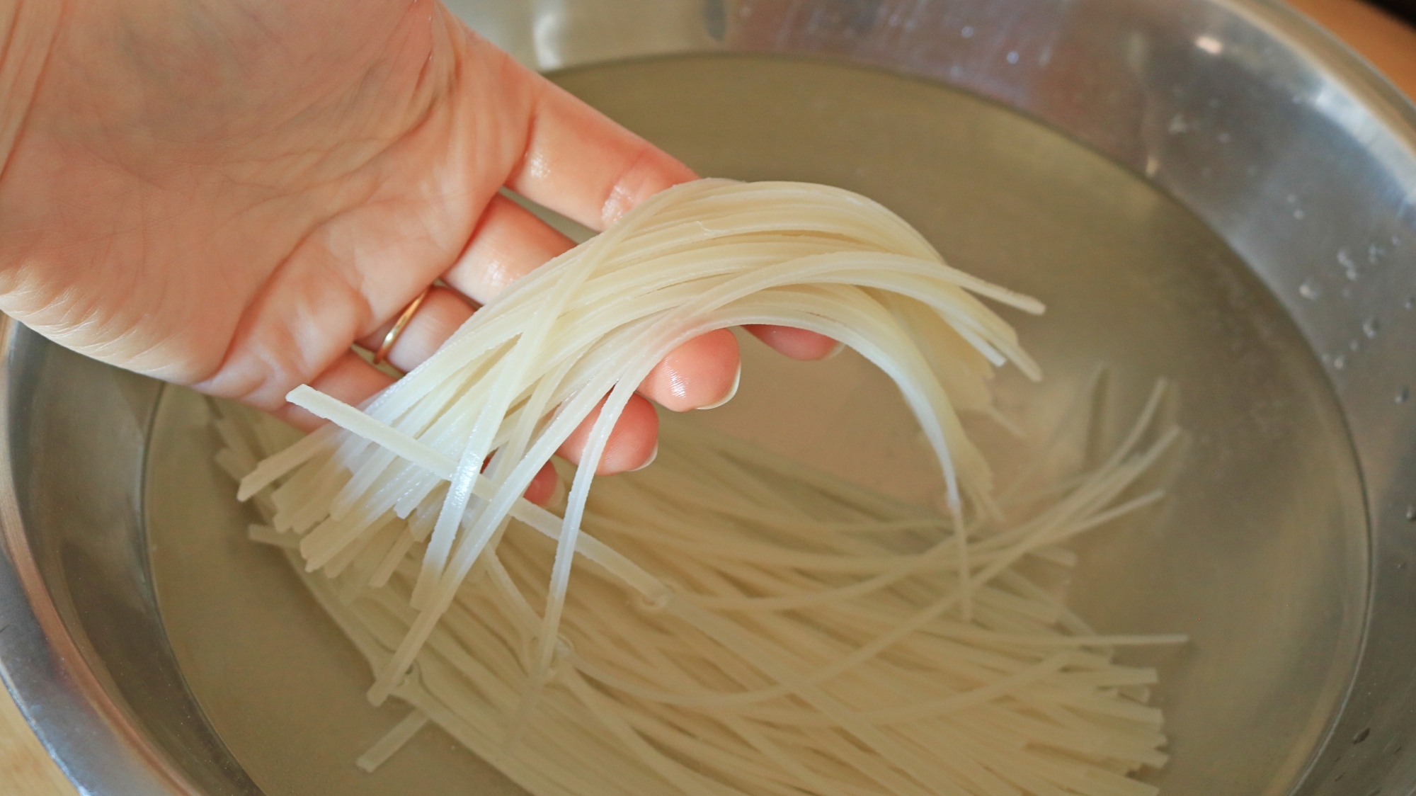 Uma mão segurando macarrão de arroz encharcado.