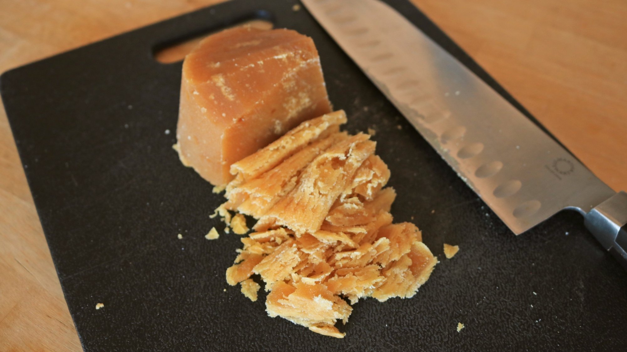 Açúcar panela picado em uma tábua preta com uma faca.