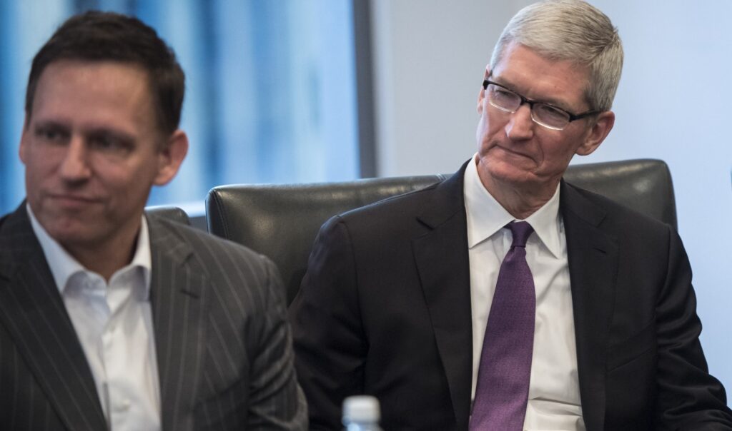 Peter Thiel e Tim Cook sentam-se em uma mesa olhando para a esquerda