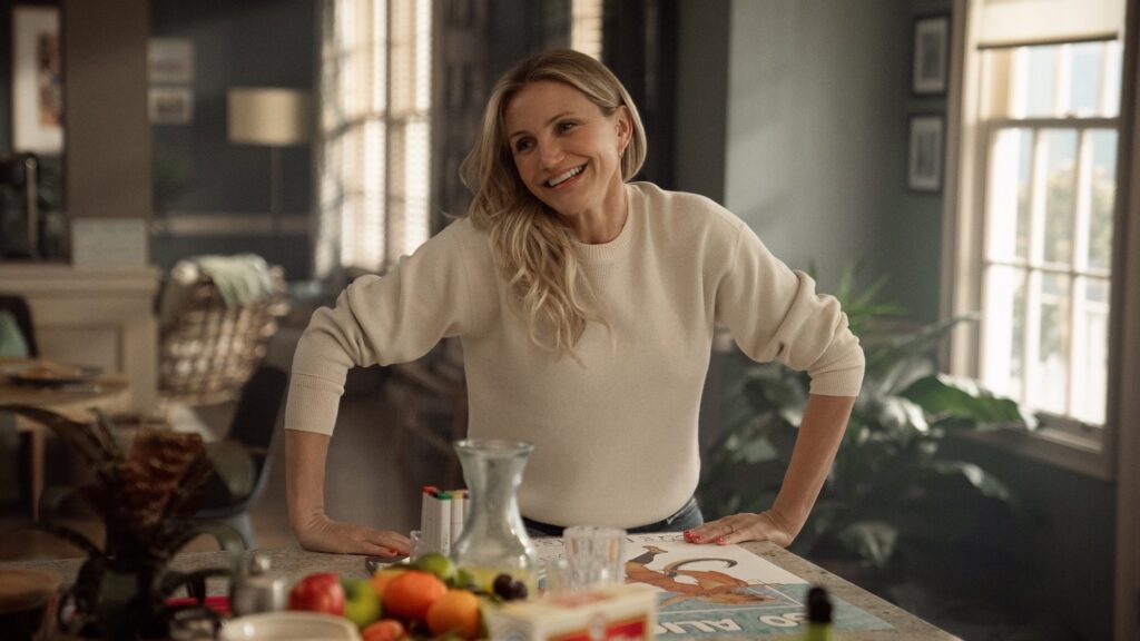 Cameron Diaz sorri em uma cozinha vestindo um suéter branco 