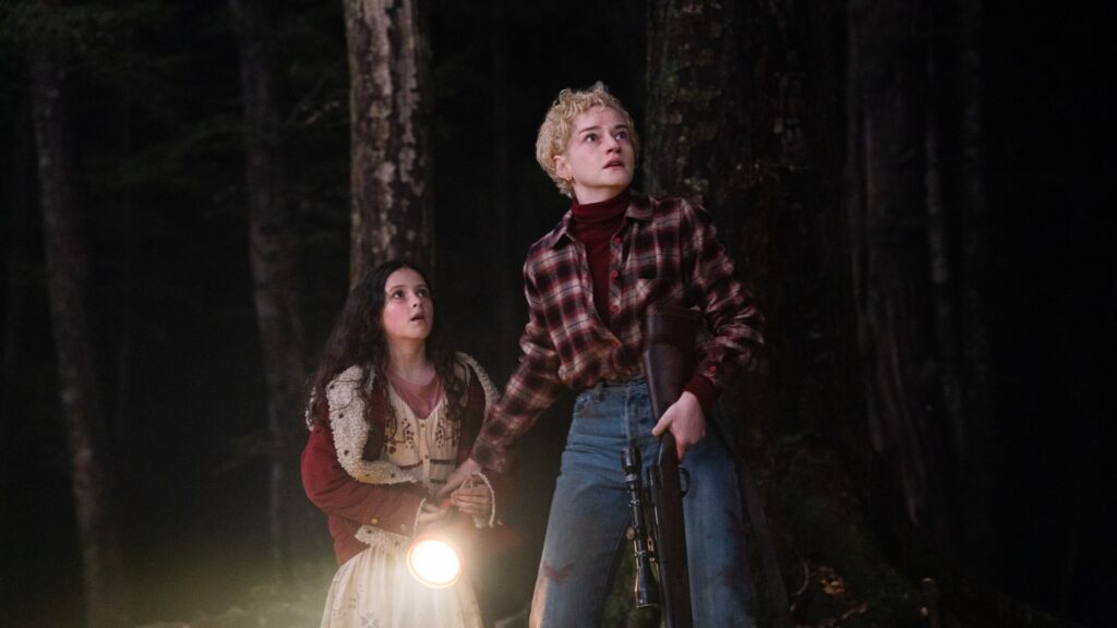 Matilda Firth e Julia Garner parecem assustadas na floresta em foto do filme Wolf Man.