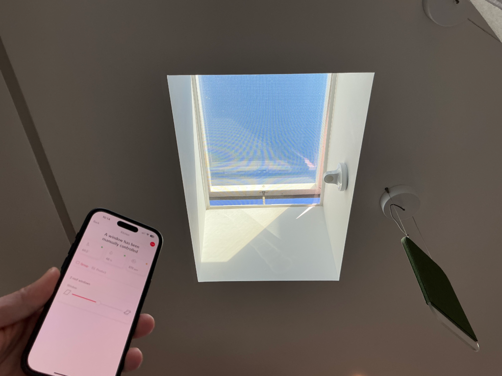 Uma janela motorizada Velux com smartphone em foto.