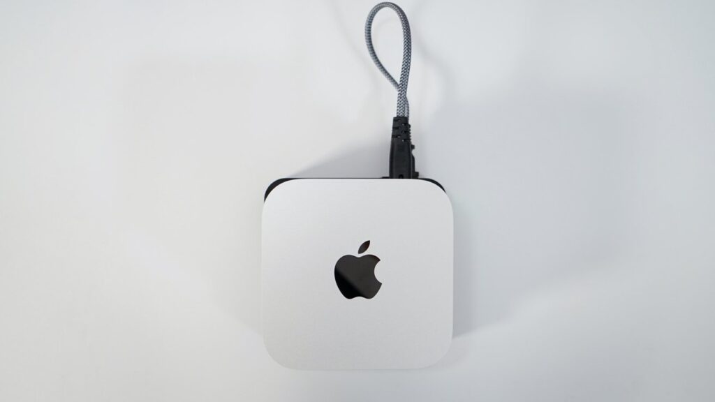 White square device with rounded corners, featuring a black apple logo on top, connected by a braided cable looped upwards.